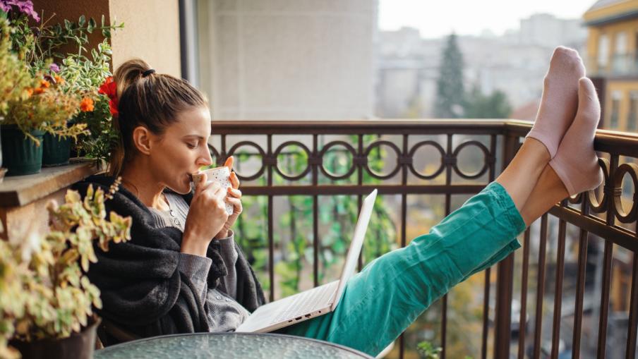 
		Eine junge Frau sitzt entspannt auf dem Balkon und arbeitet
	
